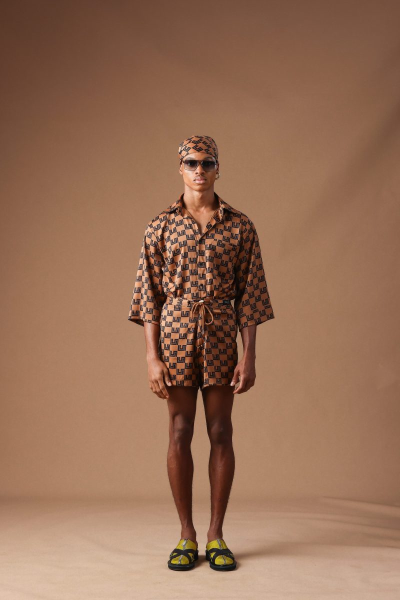 Male model in Cute Saint tan monogram-print oversized shirt, matching shorts, and headwrap with sunglasses, Rhythm of Time Collection 2025